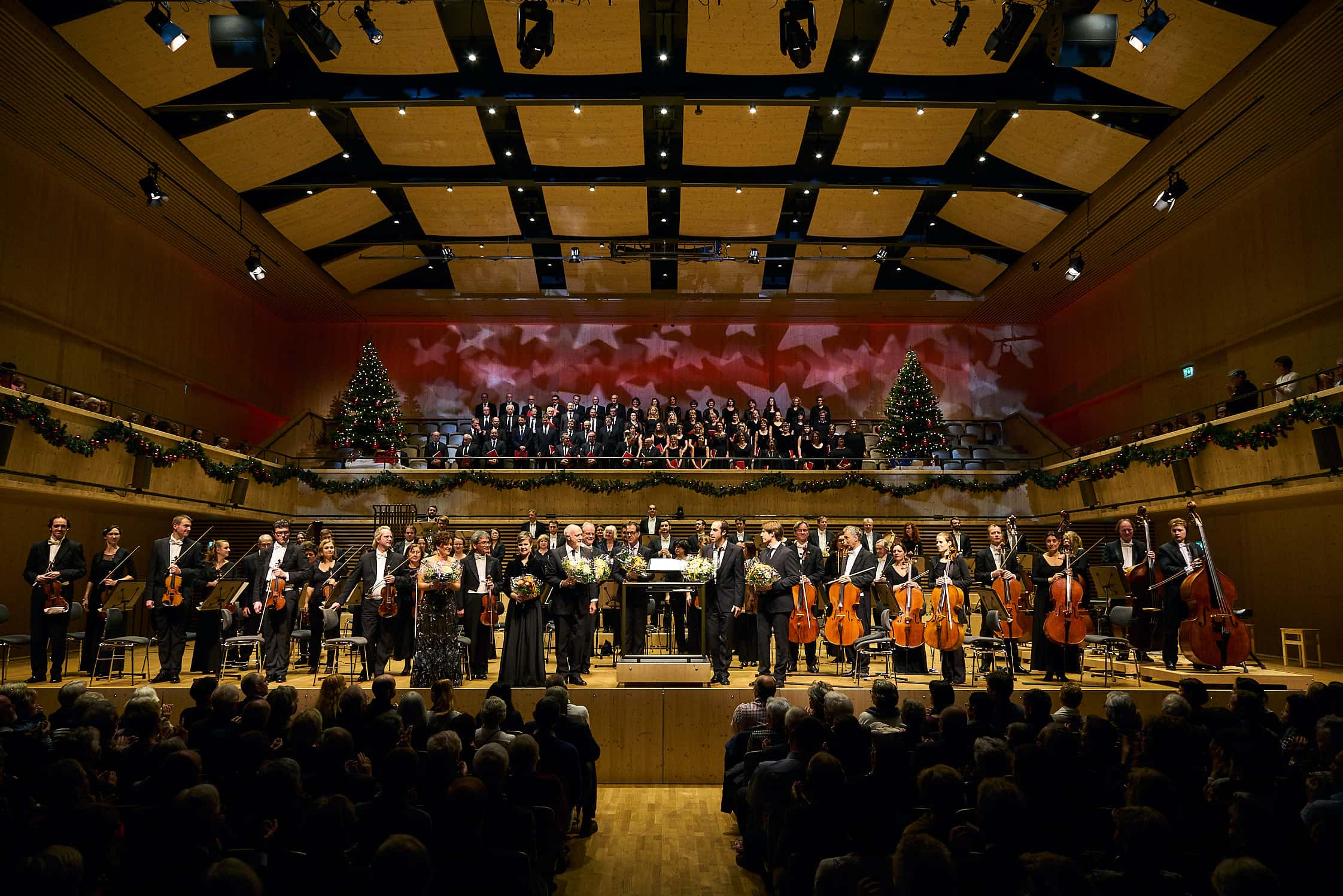 die Solisten und das gesamte Orchester empfängt stehend auf der Bühne den Schlussapplaus des Weihnachtskonzertes in der festlich geschmückten Tonhalle Maag in Zürich, die ganz aus Holz gebaut wurde.