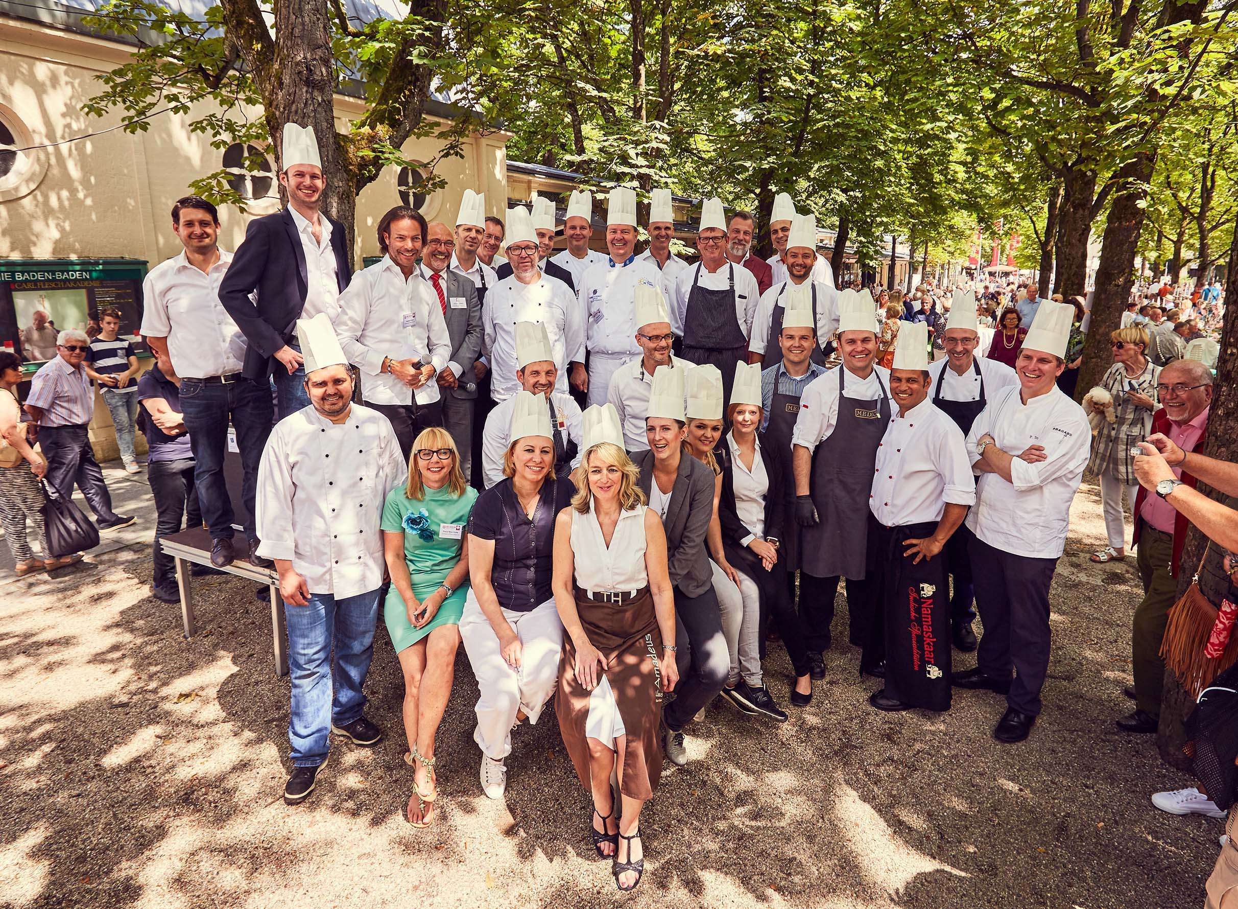 Eine große Gruppe von Köchinnen, Köchen und sonstigen Aktiven formiert sich mit Köchmützen zum Gruppenfoto und lachen in die Kamera.