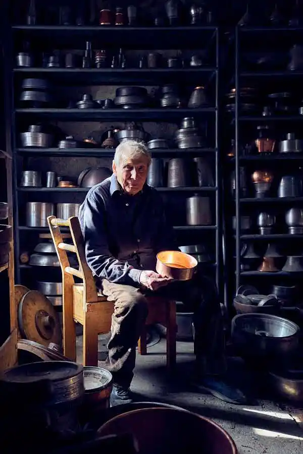 der über 80 jährige Topfmacher Nino Donnini in seiner Werkstatt auf einem Stuhl vor Regalen, die die Rotationsformen aufnimmt