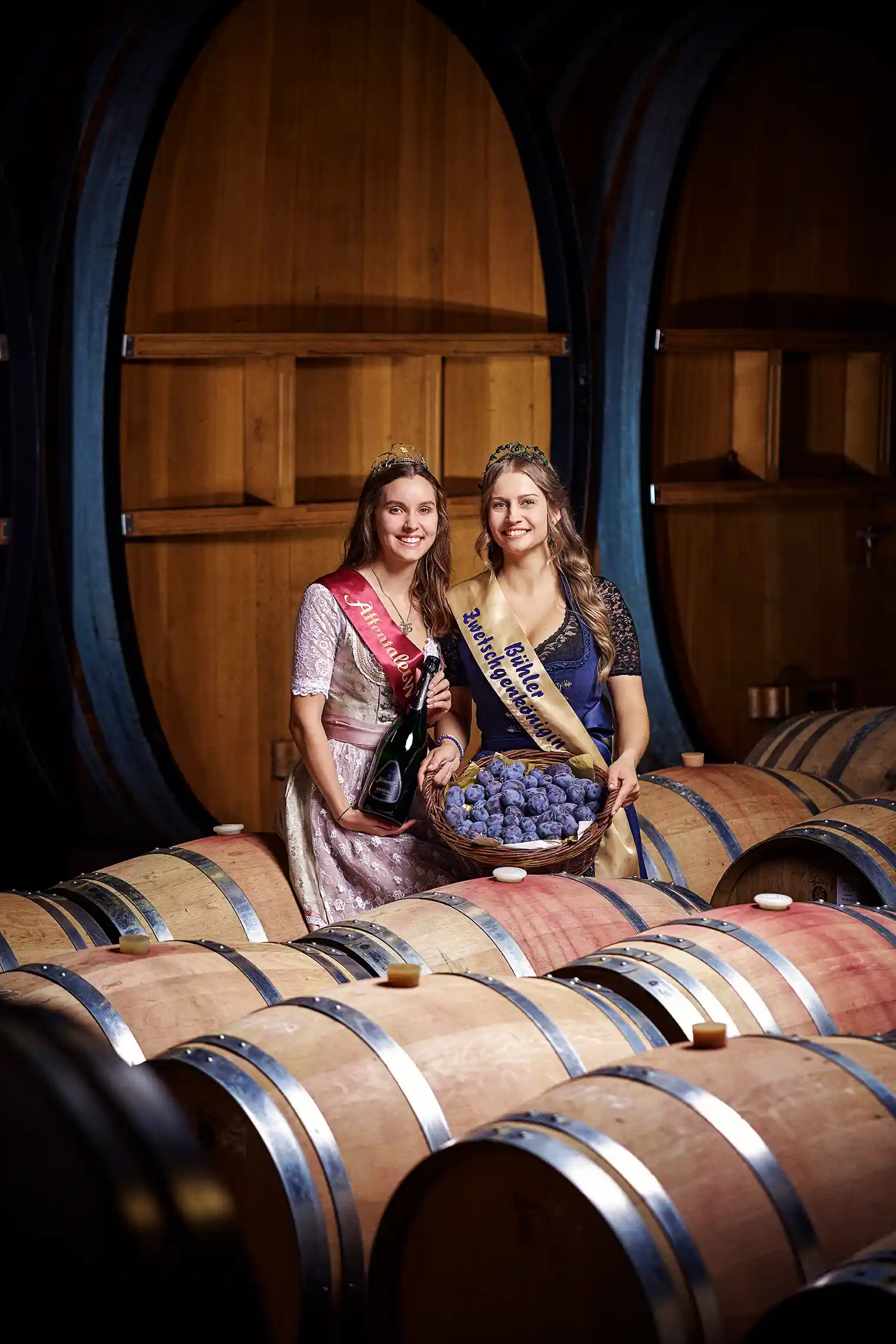 die affentaler Weinkönigin sarah I. und Alexandra I. sitzen im Fasskeller der Winzergenossenschaft und schauen vergnügt in die Kamera. das bild wurde für einen aufsteller bei Zwetschgenfest fotografiert um für eine gemeinsame Aktion der beiden Hoheiten zu werben.